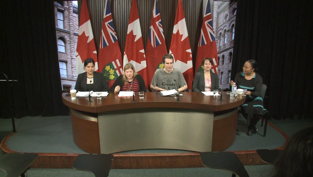 Picture of speakers seated behind a desk inside the Queens Park press room